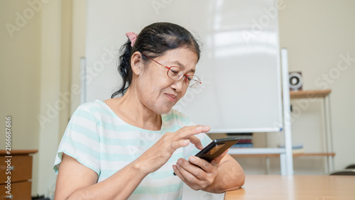 Asian senior woman enjoy using smartphone learning technology AI chat bot at home in vacation, or concept online shopping, browsing internet and communication. Lifestyle health. Elderly female glasses