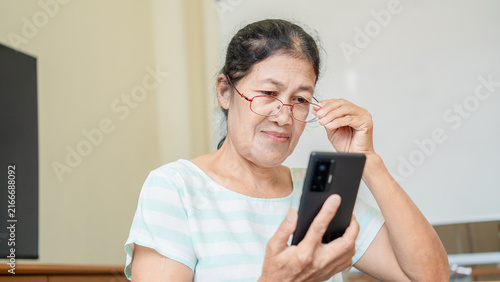 Photography Elderly Asian woman using smartphone while adjusting glasses, Senior female using technology and with nearsighted or farsightedness, eye diseases