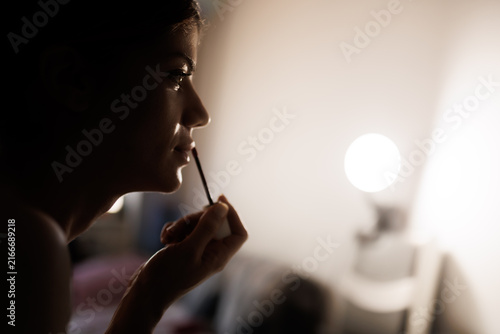 Fotografie Girl applying makeup in front of a mirror using a pencil in a bright room during