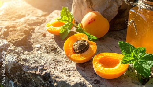 Fresh apricots and jam jar on rustic stone surface.
