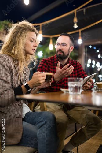 Casual conversation over coffee in a cozy cafe setting, with a thoughtful young man and woman engaged in a lively discussion, highlighting social interaction and a relaxed atmosphere.