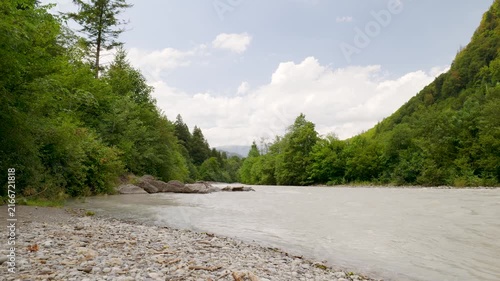 Milky glacial river flowing through a lush green valley on a partly cloudy day. Switzerland
