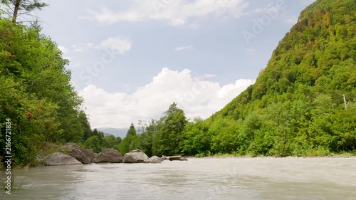Muddy river water flowing through a verdant forest gorge on a sunny day. Switzerland