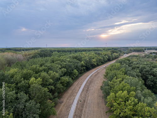 Foto Cycling path curving along a flood dyke through green floodplain forest under a