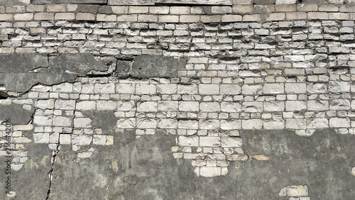 Obraz na plátne Close‑up of a heavily weathered brick wall with deteriorating plaster, exposed masonry, cracks, and missing sections, creating a rugged urban decay texture with strong architectural character