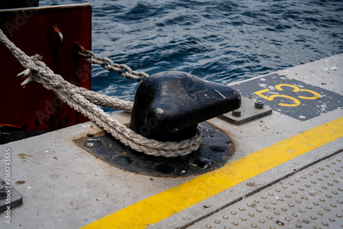 Konstfotografi Heavy black mooring bollard tied with thick rope on concrete pier near blue sea water