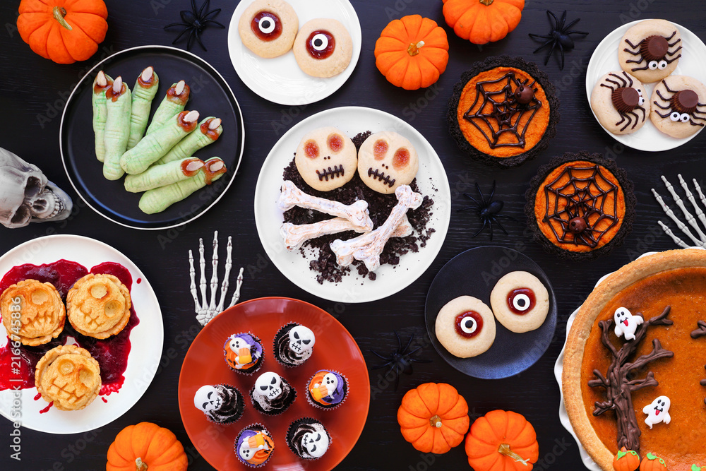 Fototapeta premium Fun Halloween dessert table scene over a black wood background. Top view. Selection of cookies, cupcakes and pumpkin and apple tarts and pies.
