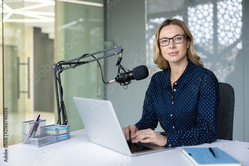 Obraz na płótnie Woman recording a podcast episode in a modern office, seated at a desk with lapt