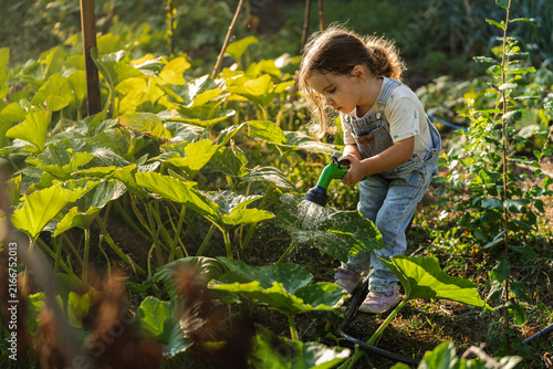 Little girl waters plants with a garden hose