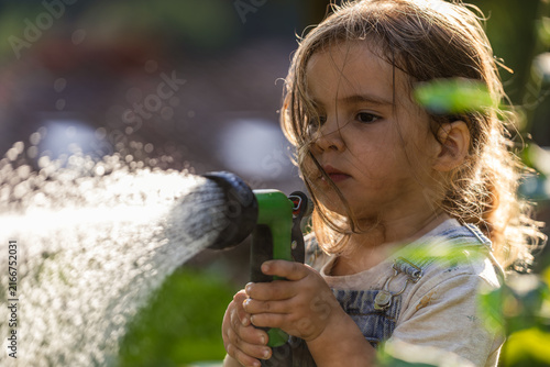 Little girl waters garden with focused expression