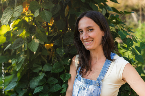 Woman smiles gently, standing amidst lush green leaves