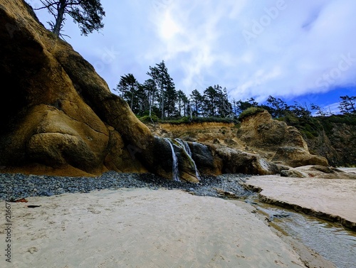 Foto A small freshwater cascade spills down sculpted sandstone cliffs onto a broad sa