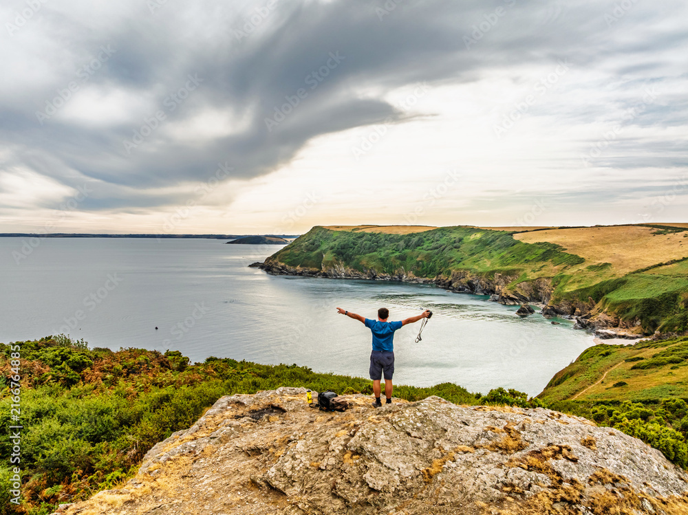 Naklejka premium Men on rocks over Cornwall Cliffs and Farms from a drone, Polruan, Cornwall, England