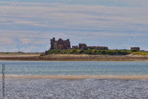 Cuadro en lienzo Ruined stone castle standing on a low coastal island beyond tidal flats and shallow water beneath a partly cloudy sky