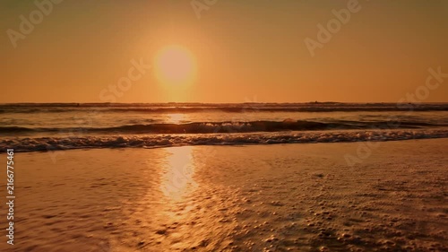 Golden hour sunlight casts a warm glow over gentle ocean waves as they roll onto a wet sandy beach, creating a serene and peaceful atmosphere.