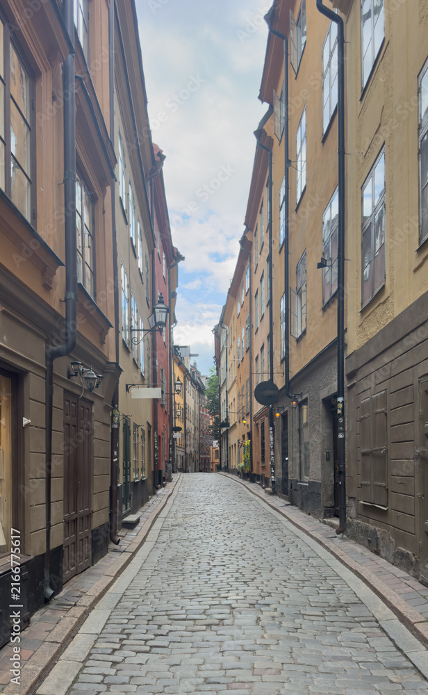 Fototapeta premium Narrow cobblestone street lined with colorful historic buildings in Gamla Stan, the old town district of Stockholm, Sweden.