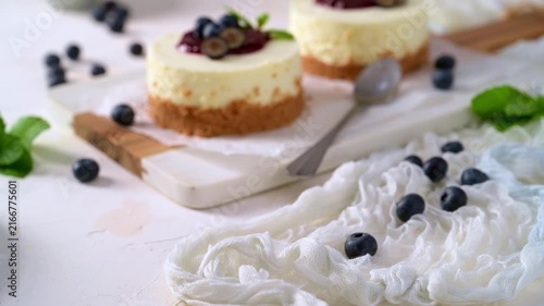 Two mini cheesecakes rest on parchment paper with vibrant berry sauce, fresh blueberries, and mint leaves, illuminated by soft natural lighting.
