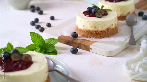 Mini cheesecakes on parchment paper feature vibrant berry sauce, fresh blueberries, and mint leaves, illuminated by soft natural lighting.
