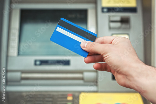 Fotografie Close-up of a man's hand holding a blue credit card in front of an automated teller machine ATM