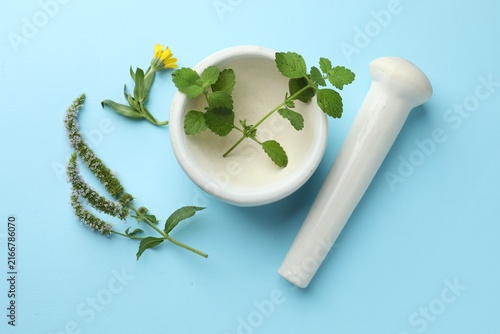Konstfotografi Mortar, pestle and herbs on light blue background, flat lay