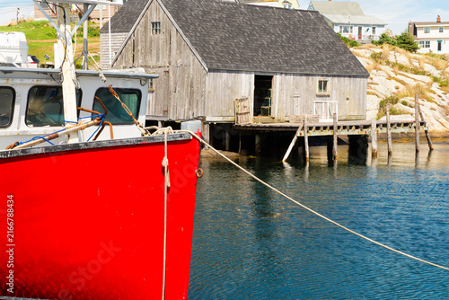 Large red boat near a weathered structure on the water in Peggy's Cove