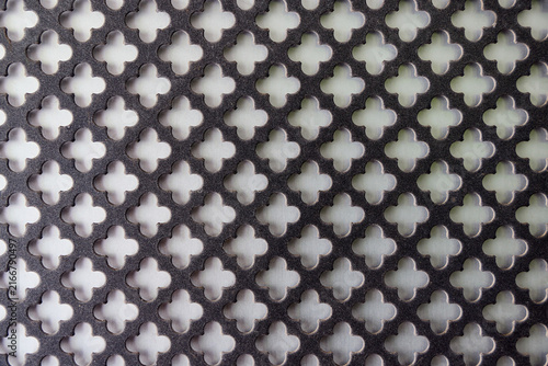 Canvas Print Perforated black metal sheet with repeating cross or clover pattern on white background, abstract geometric grid structure, industrial decorative steel panel texture, close up