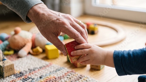 Grandfather hand giving a wooden block to a childs hand surrounded by toys