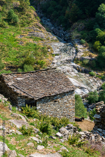 Rustic Alpine Stone Hut with Donkey and Rocky Stream on Mountain Hillside