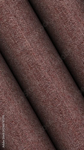 Continuous circular motion of Italian reddish brown herringbone wool silk fabric rolls revealing warm tones and soft high end apparel weave background
