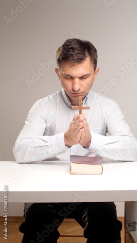 Quadro su tela man with closed eyes praying intently, holding a small wooden cross with clasped