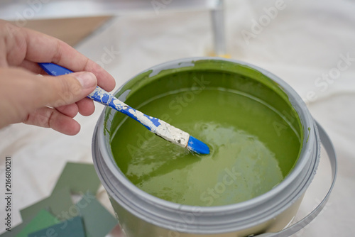 Hand mixes green paint with small brush in open paint can