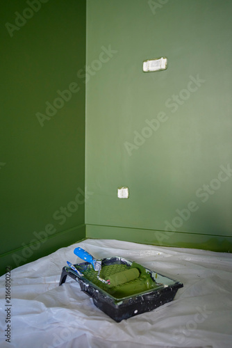 Green painted walls with paint roller and tray on protective floor covering