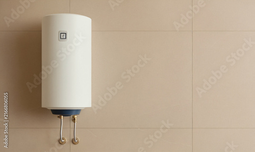 A white cylindrical water heater on a beige tiled wall.