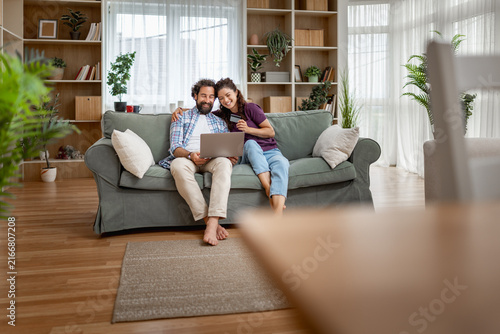 Foto Couple on sofa sharing a laptop and credit card while shopping online at home