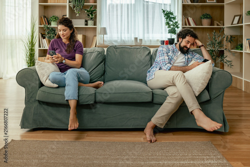 Photography Couple sitting apart on sofa using phones in bright living room