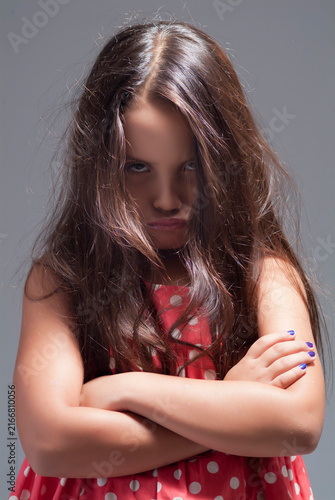 Фотография Angry young girl with arms crossed pouting and glaring at camera in red polka do