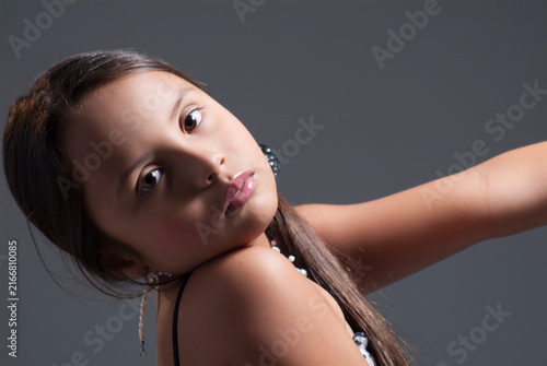 Close-up portrait of a young girl tilting her head with a thoughtful expression against a grey studio background