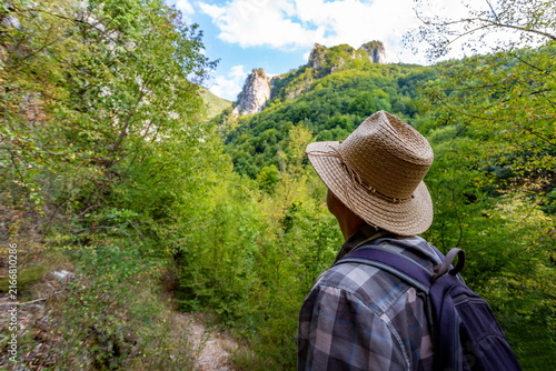 Back View of Male Hiker in Hat with Backpack Standing on Mountain Trail and Enjoying Scenic View