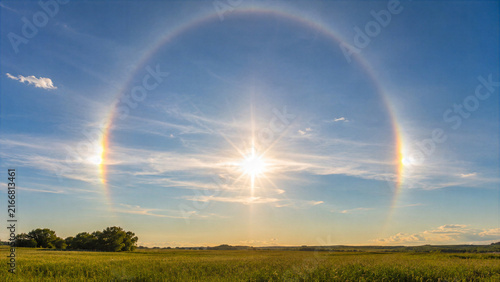 Bright sun halo with sun dogs over green grassy field