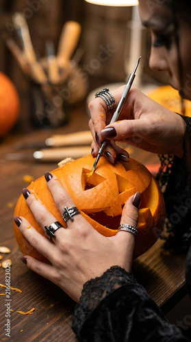 Carving a pumpkin for Halloween, a gothic woman skillfully carves a pumpkin in the shape of a jack-o'-lantern for Halloween using a professional detailing tool, pumpkin carving workshops.