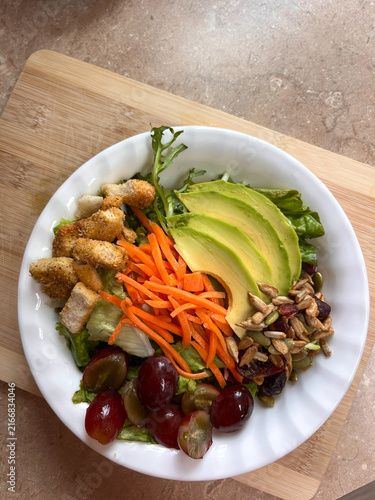 Foto Avocado Salad In White Bowl With Carrots Grapes Lettuce Croutons Seeds And Dried