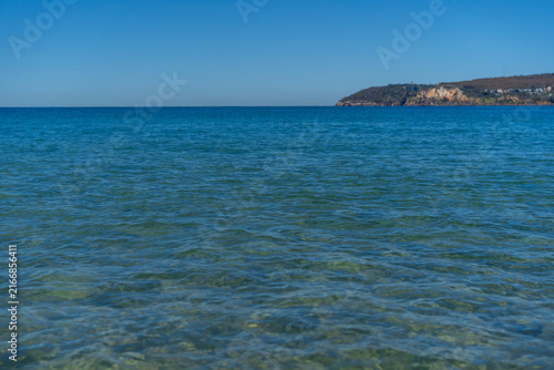 Clear ocean water with a scenic headland under blue sky.