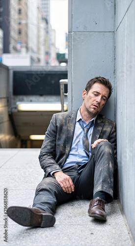 Exhausted businessman in dusty charcoal suit leaning against concrete wall outdoors on urban city street. Tired stressed male executive feeling defeated after work failure vertical shot