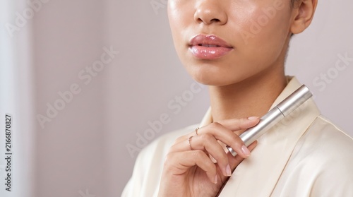Young woman applying lip gloss with glowing skin and professional makeup look