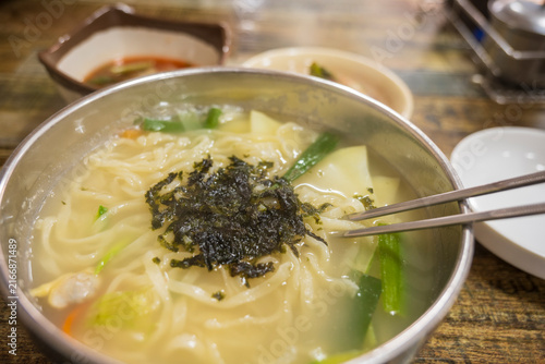 Foto Hot bowl of traditional handmade noodle soup kalguksu topped with seaweed flakes and chopsticks at local market eatery in South Korea