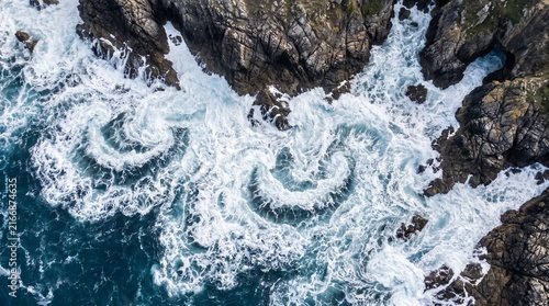 Top down aerial view of swirling ocean waves creating patterns against rocks