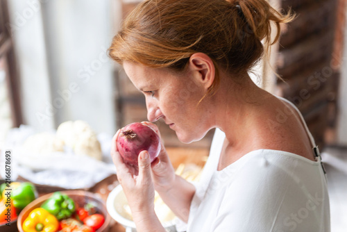 Fotografie Person smelling a red onion in a kitchen with fresh vegetables.