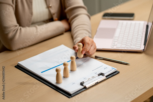 Hand placing wooden figures on financial chart with laptop and pen on wooden desk