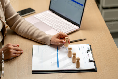 Hand placing wooden figurine on financial chart with laptop and pen on wooden desk