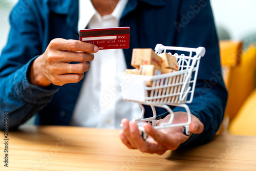 Person holding credit card and miniature shopping cart filled with parcel boxes